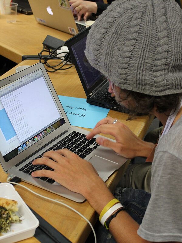 A student in a beanie coding at a hackathon in Zurich